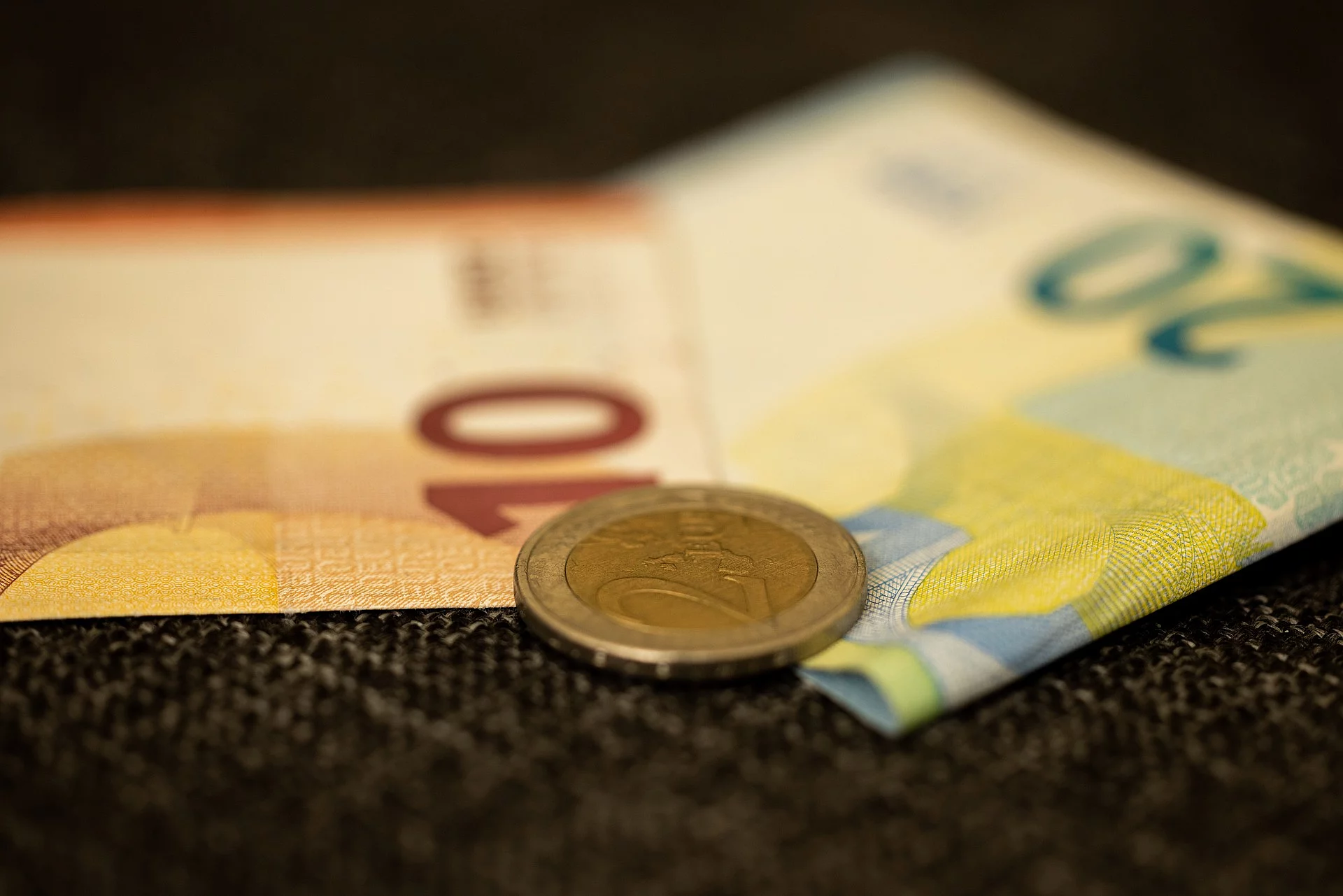 Eine Euromünze liegt auf einem 10 und einem 20 Euroschein