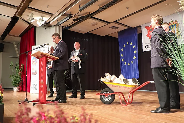 Oststeinbeks Wehrführer Carsten Steffen übergibt Geschenke - eine Schubkarre voller Konserven für das Team. Foto: Stadt Glinde