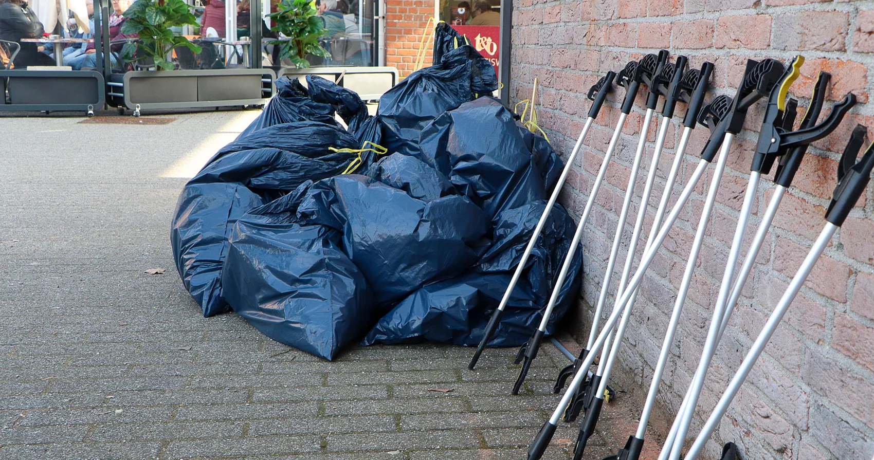Mehrere Müllbeutel und Müllzangen stehen an einer Wand.