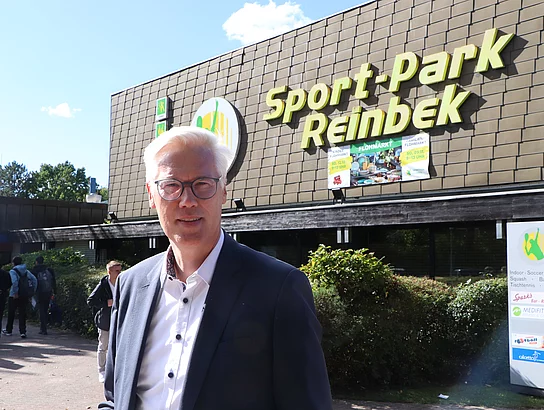 Bürgermeister Reinhard Zug lächelt vor dem Eingang des Sportpark Reinbek