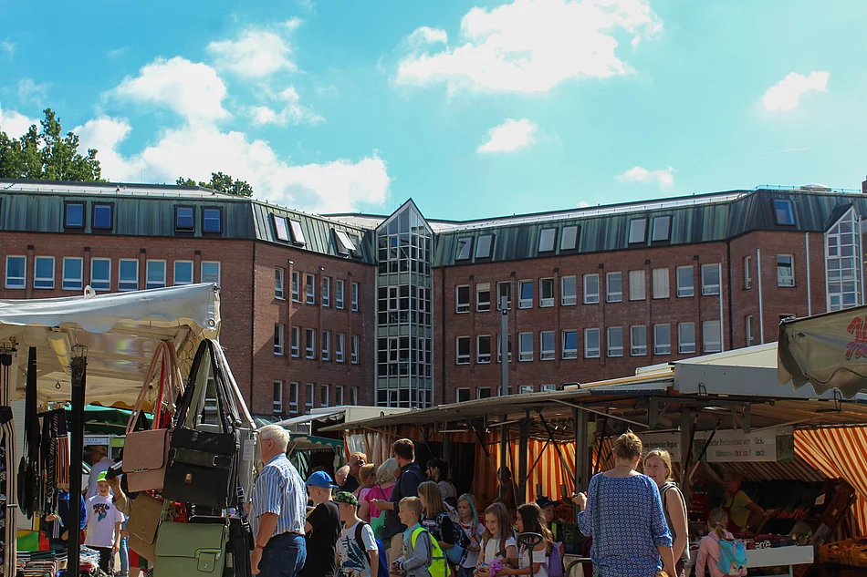 Auf dem Glinder Wochenmarkt fällt die Auswahl schwer, weil das Angebot groß ist. Wochenmarktstände mit Handtaschen und ein Stand mit Gemüse. Besucher schauen sich um.