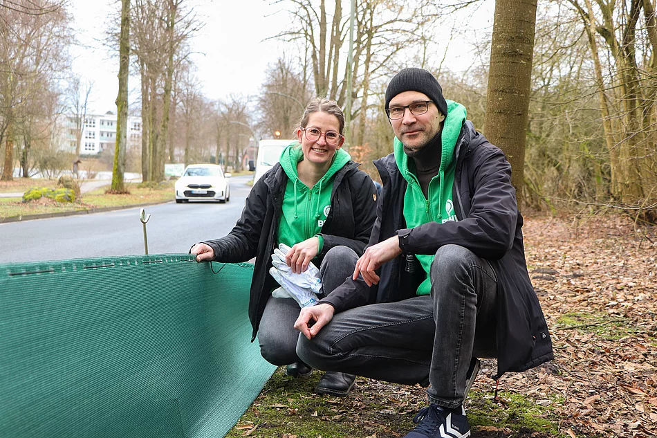 Eine Frau und ein Mann knieen neben einem Krötenschutzzaun.