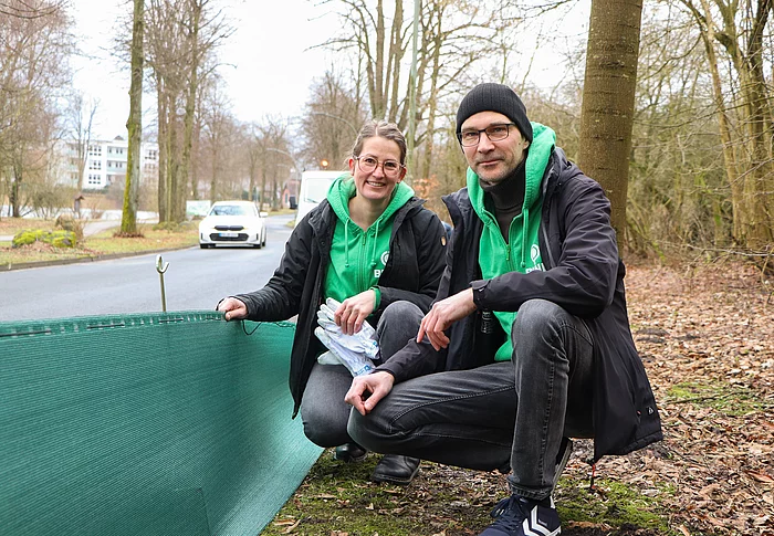 Eine Frau und ein Mann knieen neben einem Krötenschutzzaun.