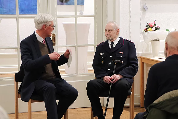 Rainhard Zug im Gespräch mit Siegfried Kraft, der eine Feuerwehr-Uniform trägt.