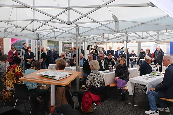 In einem Zelt sitzen Menschen an Tischen mit weißen Tischdecken.