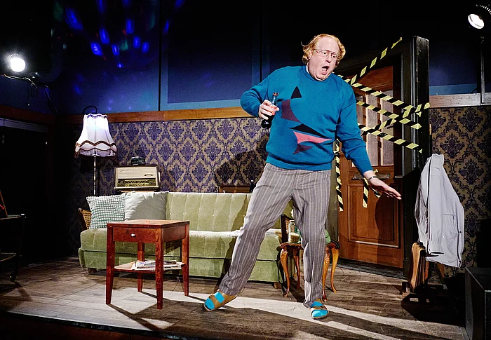 Ein Mann mit blauem Pullover tanzt in einem Wohnzimmer.