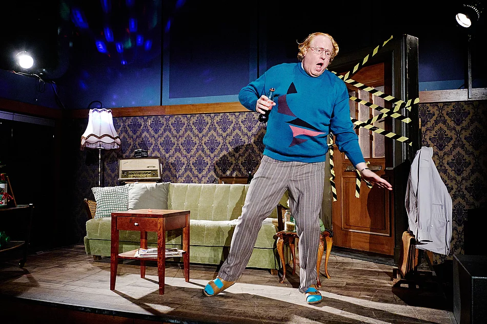 Ein Mann mit blauem Pullover tanzt in einem Wohnzimmer.