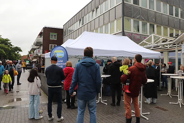 Vor einem weißen Zelt stehen Menschen, um die Fairtrade-Stadt-Verleihung zu sehen.