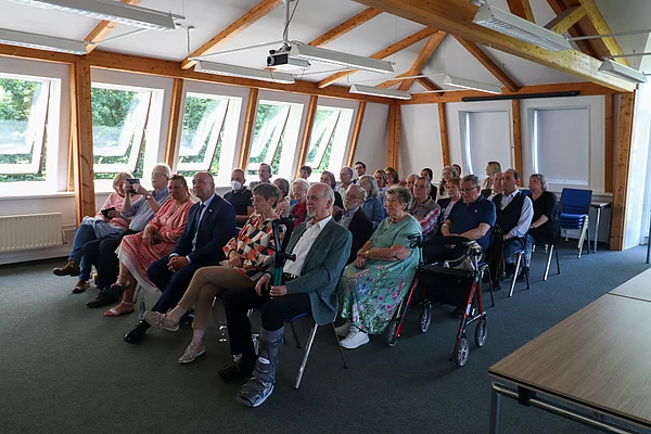 Publikum sitzt auf Stühlen und schaut nach vorn. 