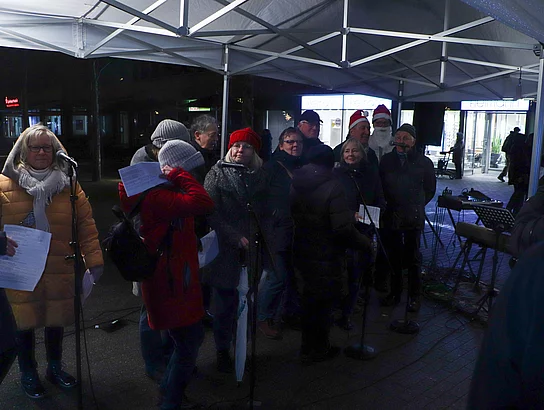 Menschen mit Weihnachtsmann-Mützen singen.