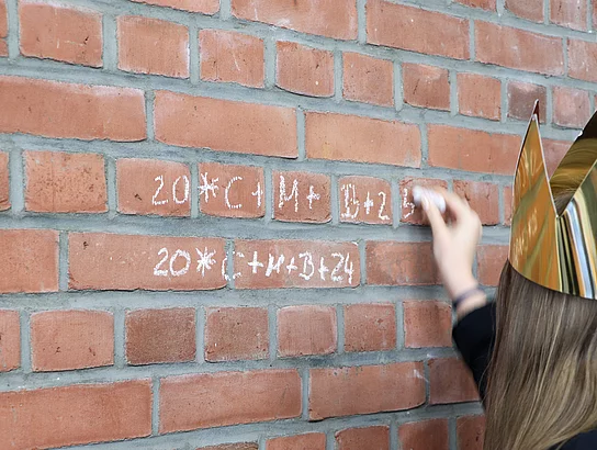 An aber Backsteinwand wird der Segensspruch der Sternsinger mit Kreide geschrieben.