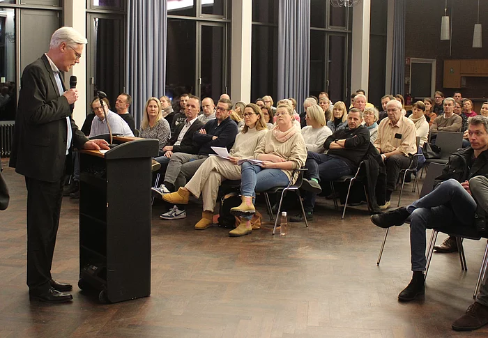 Bürgermeister Rainhard Zug steht an einem Pult vor Publikum.