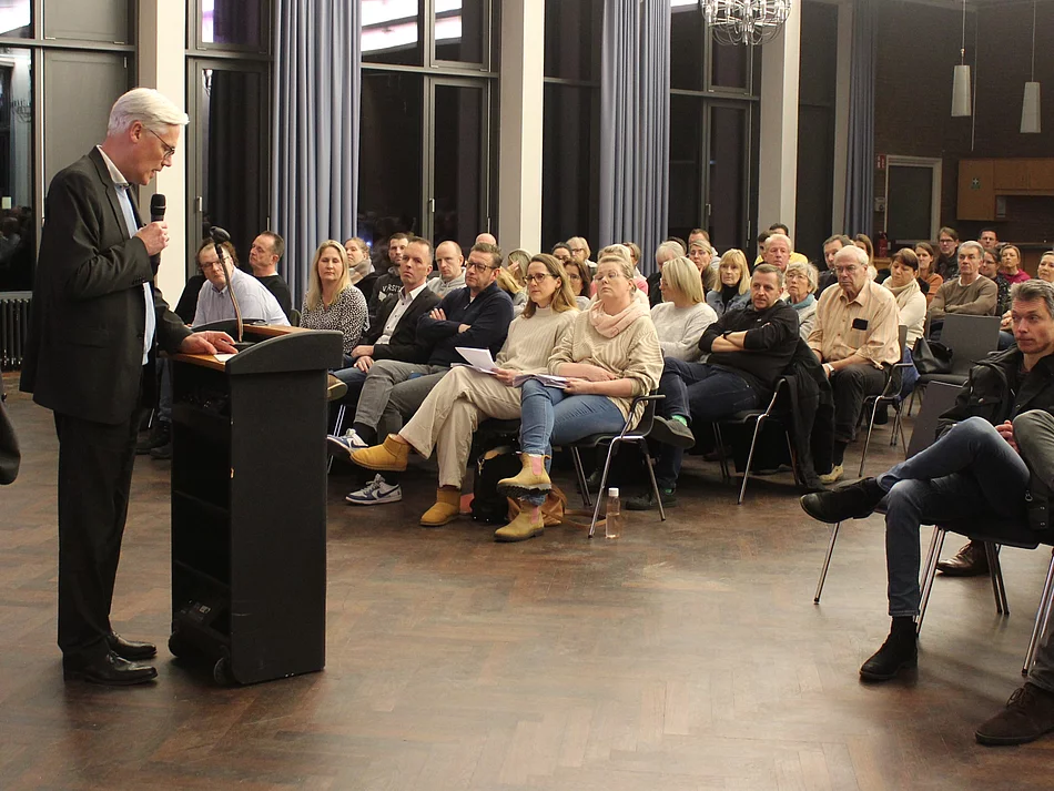 Bürgermeister Rainhard Zug steht an einem Pult vor Publikum.