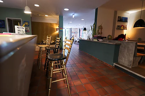 Links ein Tresen mit Stühlen und rechts ein Blick in den Raum des JUZ 24 mit Sitzgelegenheiten.