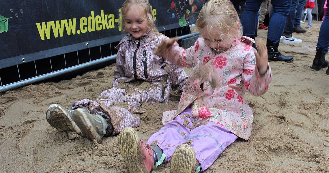 Zwei Mädchen mit Matschhose spielen im nassen Sand vor der Bühne. Foto: Stadt Glinde
