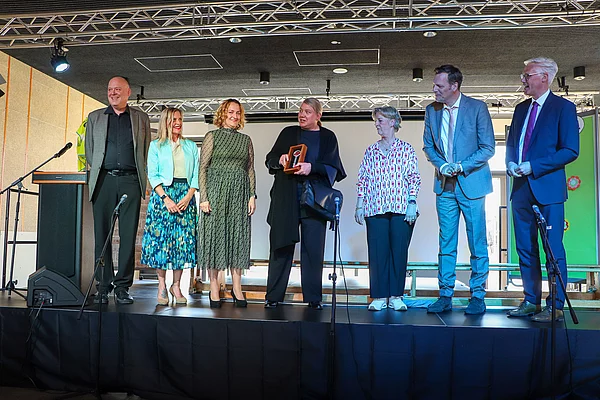 Eine Gruppe Erwachsener steht auf der Bühne und bereitet eine symbolische Schlüsselübergabe vor.