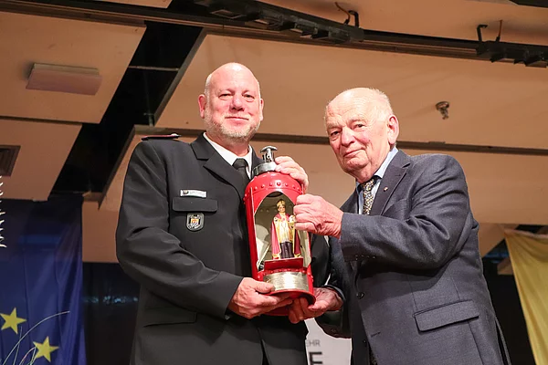 Lothar Neinass (r. früher Amt Glinde) überreicht den heiligen Antonius, der in einem offnen Feuerlöscher steht, an Wehrführer Michael Weidemann. Foto: Stadt Glinde