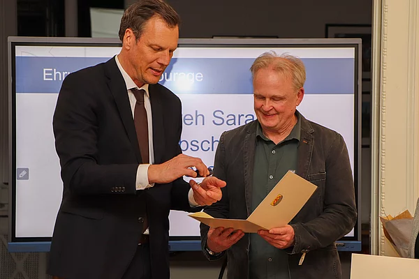 Bürgervorsteher Claus Peters übergibt eine Ehrennadel an einen Mann.