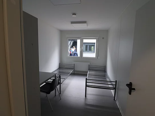 In einem schmalen Raum stehen zwei Betten ohne Matratze. 