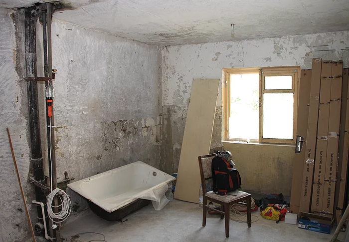 Ein Zimmer wird umgebaut. Leitungen sind zu sehen, die Wände sind unverputzt. Eine Badewanne steht im Raum.