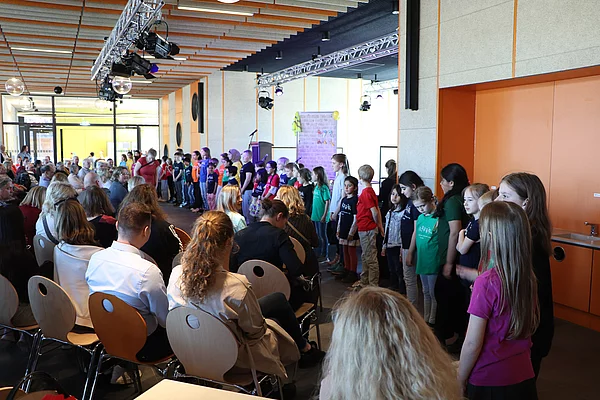 Eine Gruppe Kinder steht vor einer Bühne und singt.