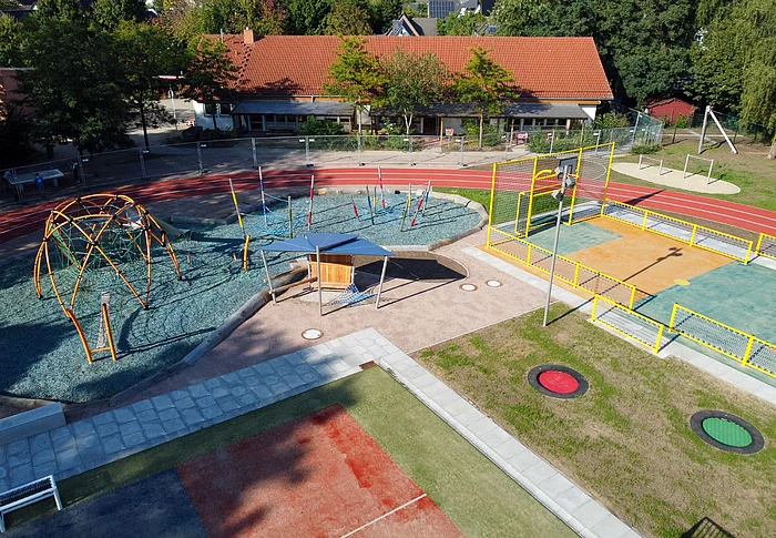 Ein Sportplatz mit vielen Spielgeräten, wie Reck, Trampolin, Klettergerüst - von oben fotografiert.