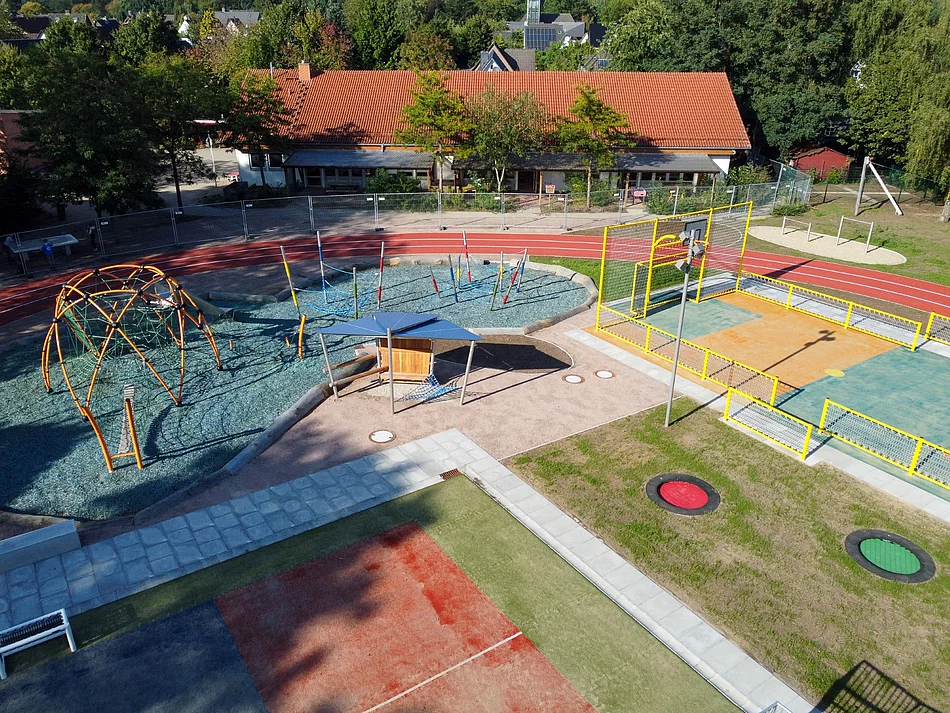 Ein Sportplatz mit vielen Spielgeräten, wie Reck, Trampolin, Klettergerüst - von oben fotografiert.