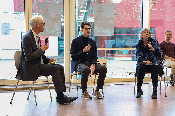 Drei Personen sitzen auf Stühlen in einer Gesprächsrunde 