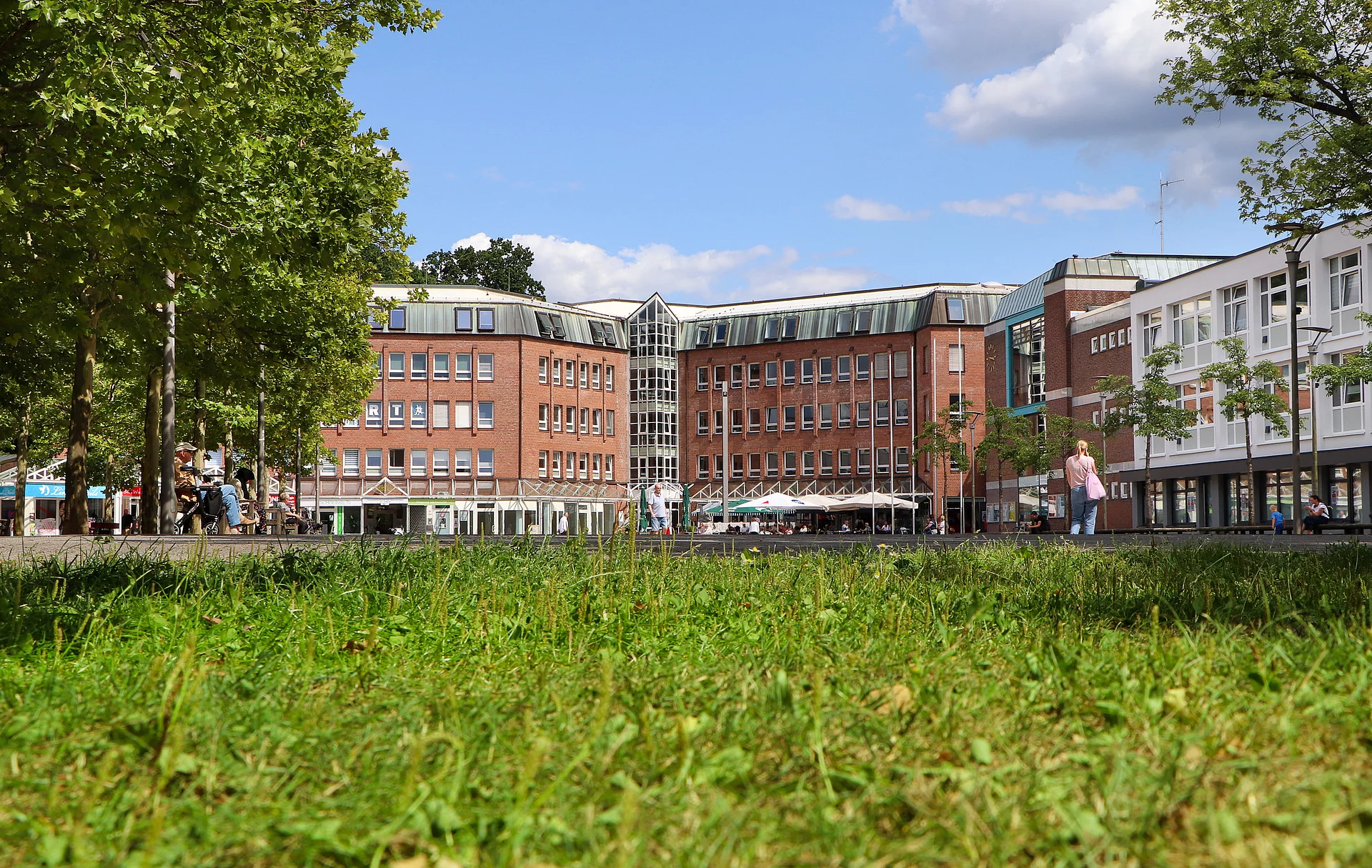 Im Vordergrund eine grüne Wiese, im Hintergrund das Rathaus, davor der Markt mit Menschen.