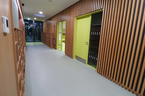 Die Klassenräume im Obergeschoss haben grüne Türen und daneben ein Fenster. An den Flurwänden sind viele Holzelemente verbaut.