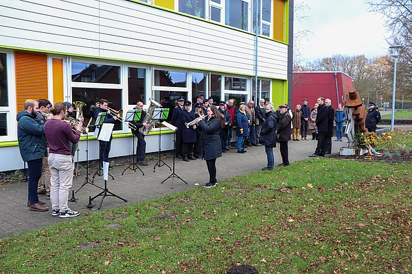 Der Posaunenchor und eine Gruppe Menschen stehen am Mahnmal für die Opfer des Zwangsarbeitslagers Wiesenfeld. 