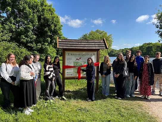 Schülerinnen und Schüler stehen an einem Schild am Mühlenteich.