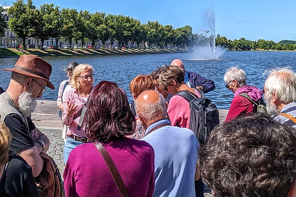 Eine Menschengruppe schaut auf einen See mit einer Fontaine.