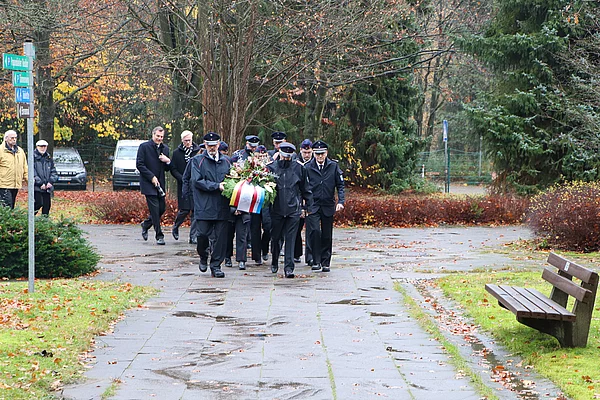 Kameradinnen und Kameraden der Freiwilligen Feuerwehr Glinde tragen einen Gedenkkranz auf dem Friedhof