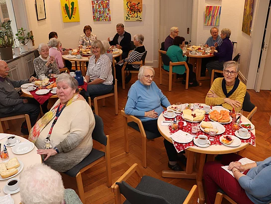 An weihnachtlichen Tischen sitzen Menschen und frühstücken.