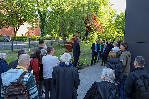 Eine Gruppe steht mit gesenkten Köpfen am Mahnmal.