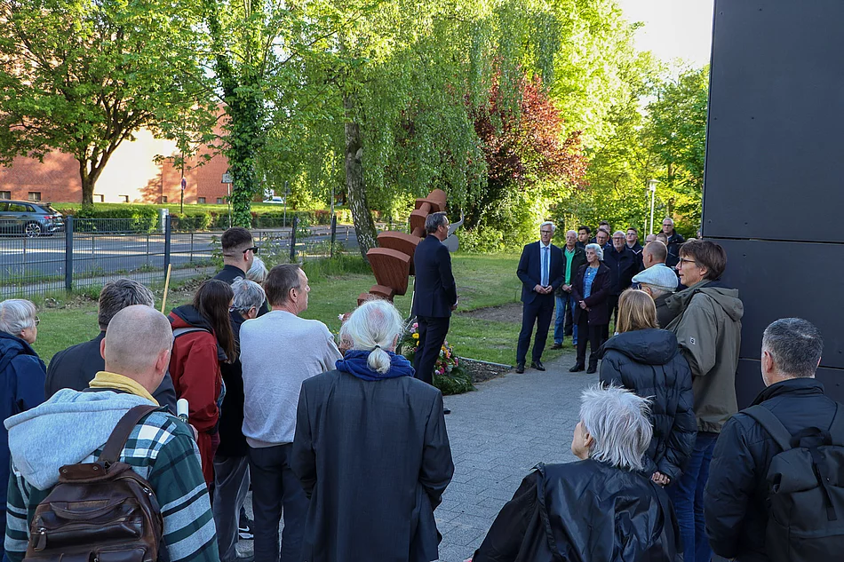 Eine Gruppe steht mit gesenkten Köpfen am Mahnmal.