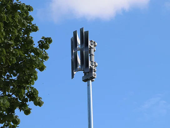 Eine Sirene auf einem Mast. Die Sirene sieht aus wie plattgedrückte Lautsprecher