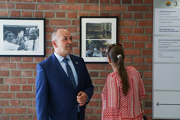 Ein Mann im blauen Jackett steht neben einer Frau mit einem roten Oberteil.