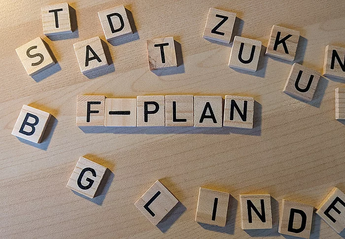 Aus kleinen Holzplättchen mit Buchstaben ist der Wort "F-Plan" gelegt