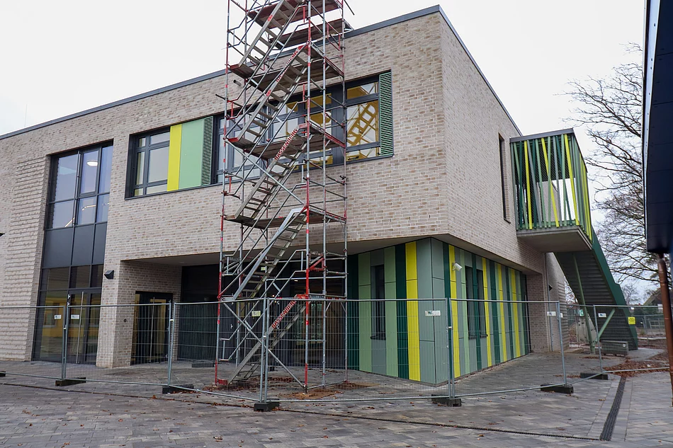 Vor einem hellen zweistöckigen Klinkersteinbau steht ein Baugerüst.