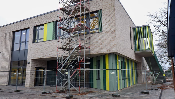 Vor einem hellen zweistöckigen Klinkersteinbau steht ein Baugerüst.
