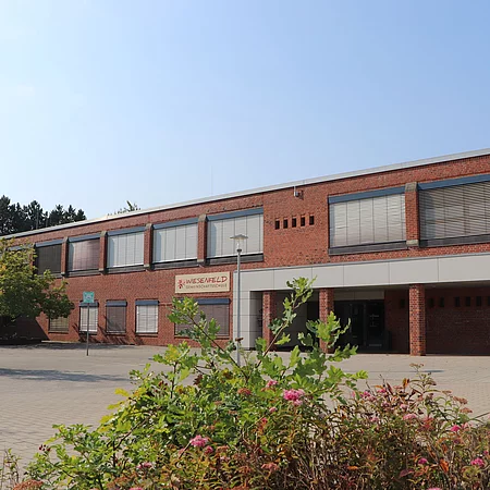Ein zweistöckiges Schulgebäude mit roten Klinkersteinen. Die Jalousien an den Fenstern sind herunter gelassen.