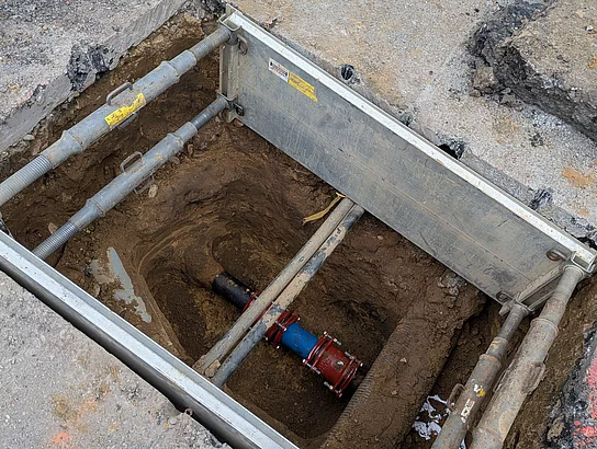 Ein Schacht im Boden, in dem eine Wasserleitung mit neuem Teilstück zu sehen ist.